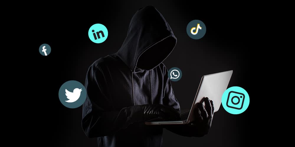A faceless man wearing a hoodie holding a laptop in an extremely dark background